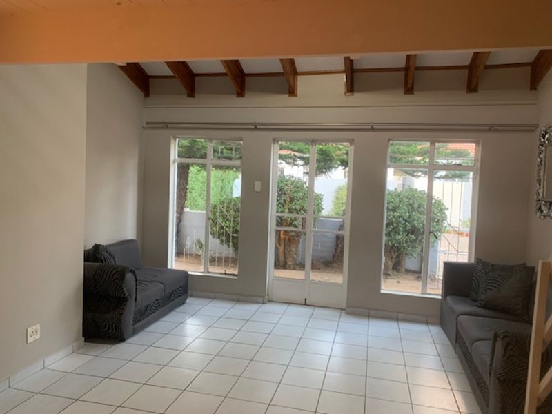 Bright living room featuring exposed timber ceiling beams, tiled flooring, and large windows providing natural light and garden views.