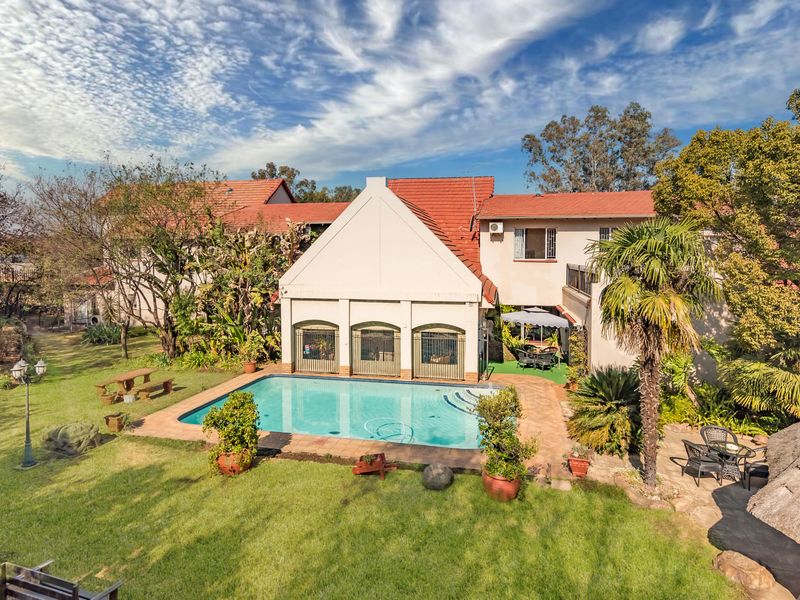 Rear view of the property featuring a swimming pool, paved patio area, and a well-maintained garden with mature trees.