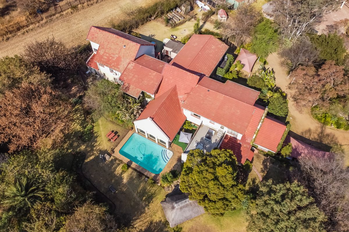 Aerial view of a residential property featuring a swimming pool, thatched lapa, and extensive garden grounds with a tiled roof structure.