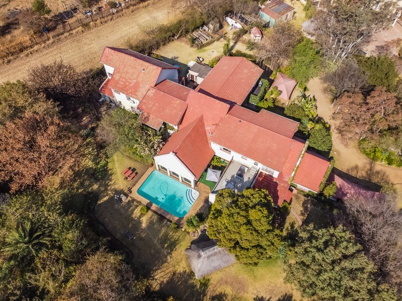 Aerial view of a residential property featuring a swimming pool, thatched lapa, and extensive garden grounds with a tiled roof structure.