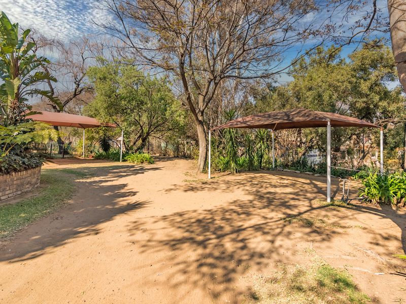Spacious garden area featuring mature trees, established landscaping, a brick retaining wall, and two installed shade sails providing outdoor coverage.