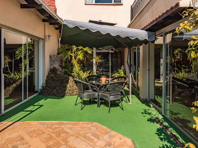 A covered patio area featuring sliding glass doors, tiled flooring, and artificial turf, providing a functional outdoor entertainment space.