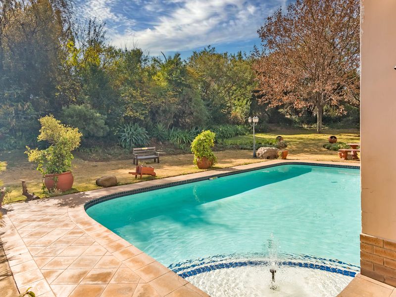 A well-maintained swimming pool area featuring a tiled surround, integrated water fountain, and a spacious, landscaped garden backdrop.
