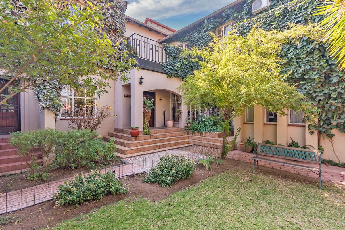 A charming rear exterior view featuring a tiled patio, a balcony with wrought iron railings, and established garden landscaping against the building facade.