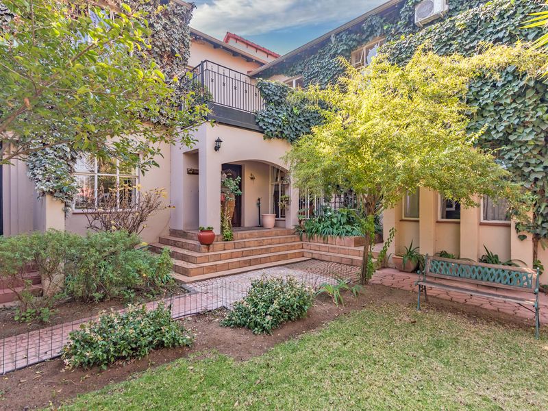 A charming rear exterior view featuring a tiled patio, a balcony with wrought iron railings, and established garden landscaping against the building facade.