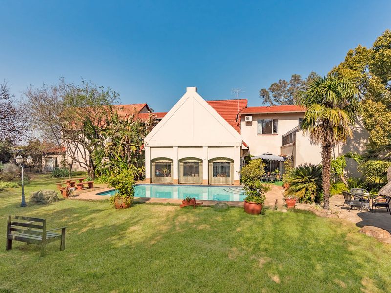 Rear view of the property featuring a swimming pool, well-maintained garden, and traditional architectural roofline.