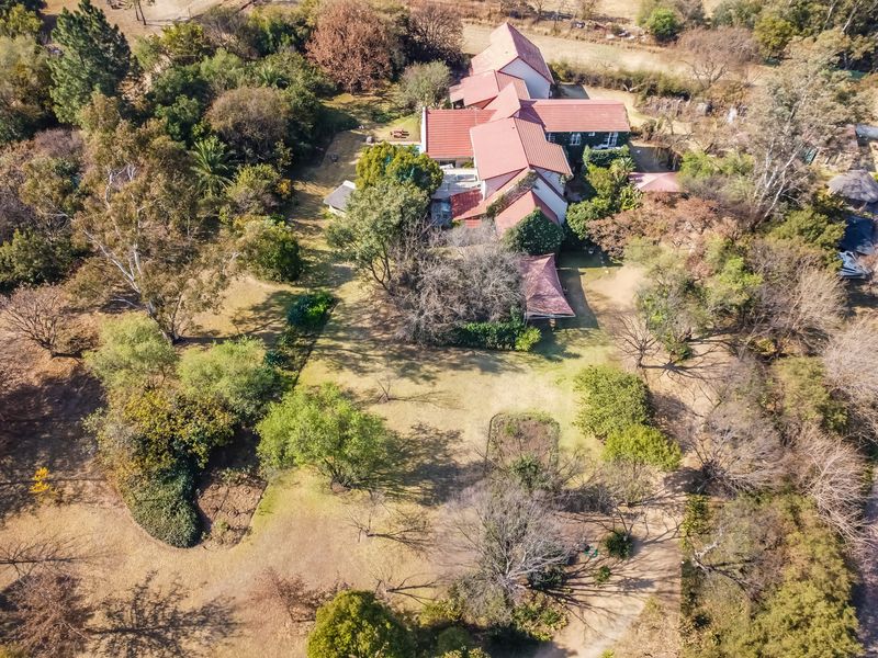 An aerial view of a large residential property featuring a multi-pitched tiled roof, extensive landscaped grounds, and mature trees.