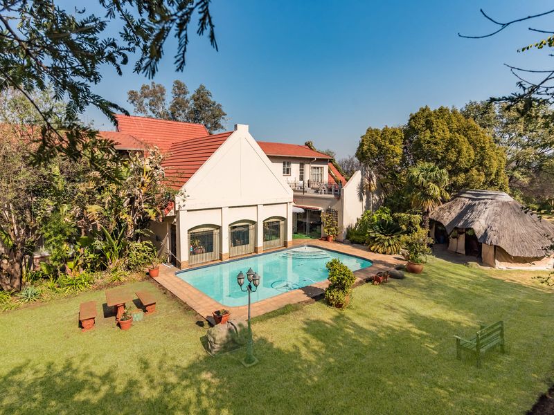 Rear view of the property featuring a swimming pool, paved patio area, landscaped garden, and a traditional thatched lapa structure.