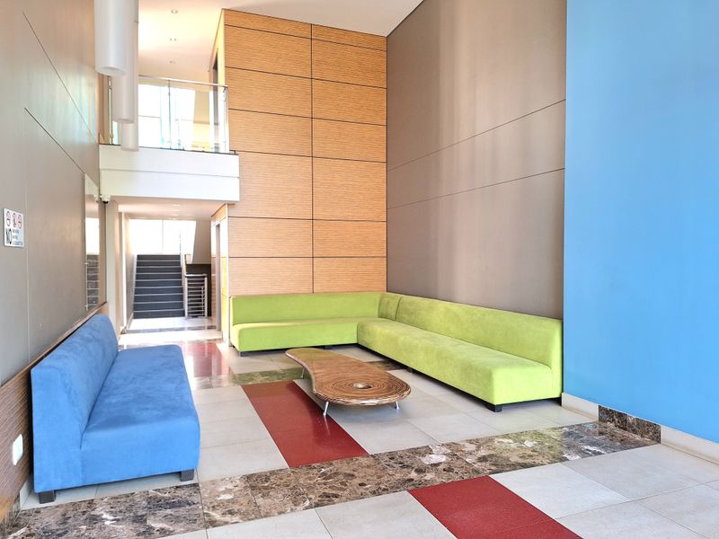 Spacious modern apartment building lobby featuring high ceilings, wood paneling, decorative tiled flooring, and a staircase with a glass balustrade.