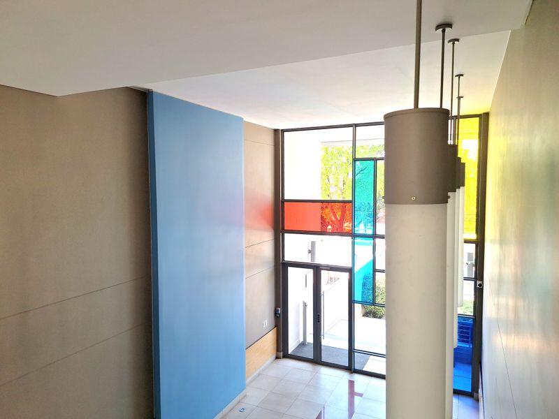 A bright and modern entrance hall featuring high ceilings, tiled flooring, and a striking stained glass window design that allows natural light to filter through.