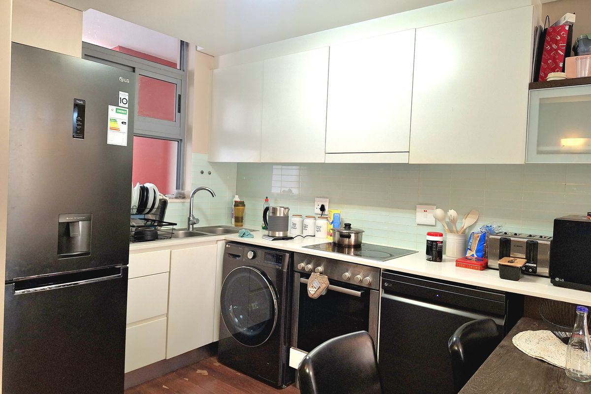 Compact modern kitchen featuring white cabinetry, tiled backsplash, integrated appliances, and a functional layout with a stainless steel sink and electric hob.
