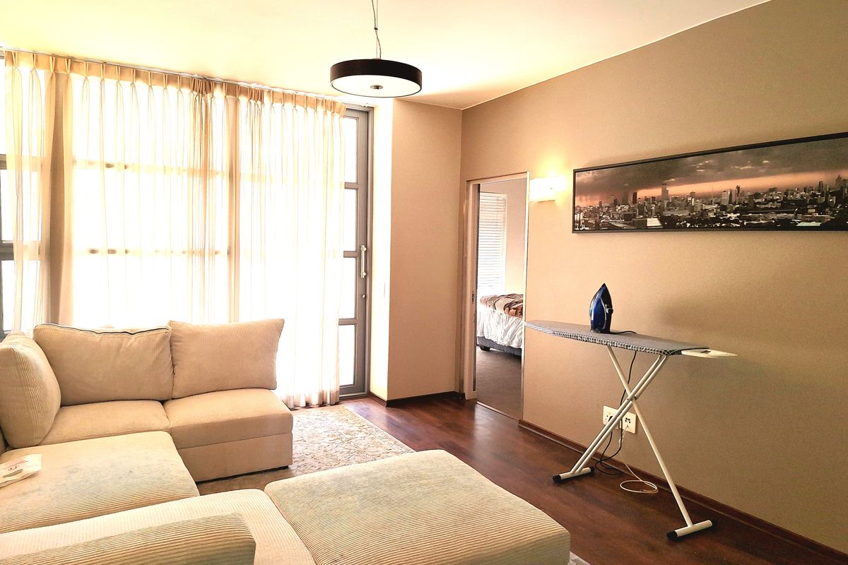 A well-maintained living room featuring laminate flooring, neutral wall tones, and a large sliding glass door providing ample natural light.
