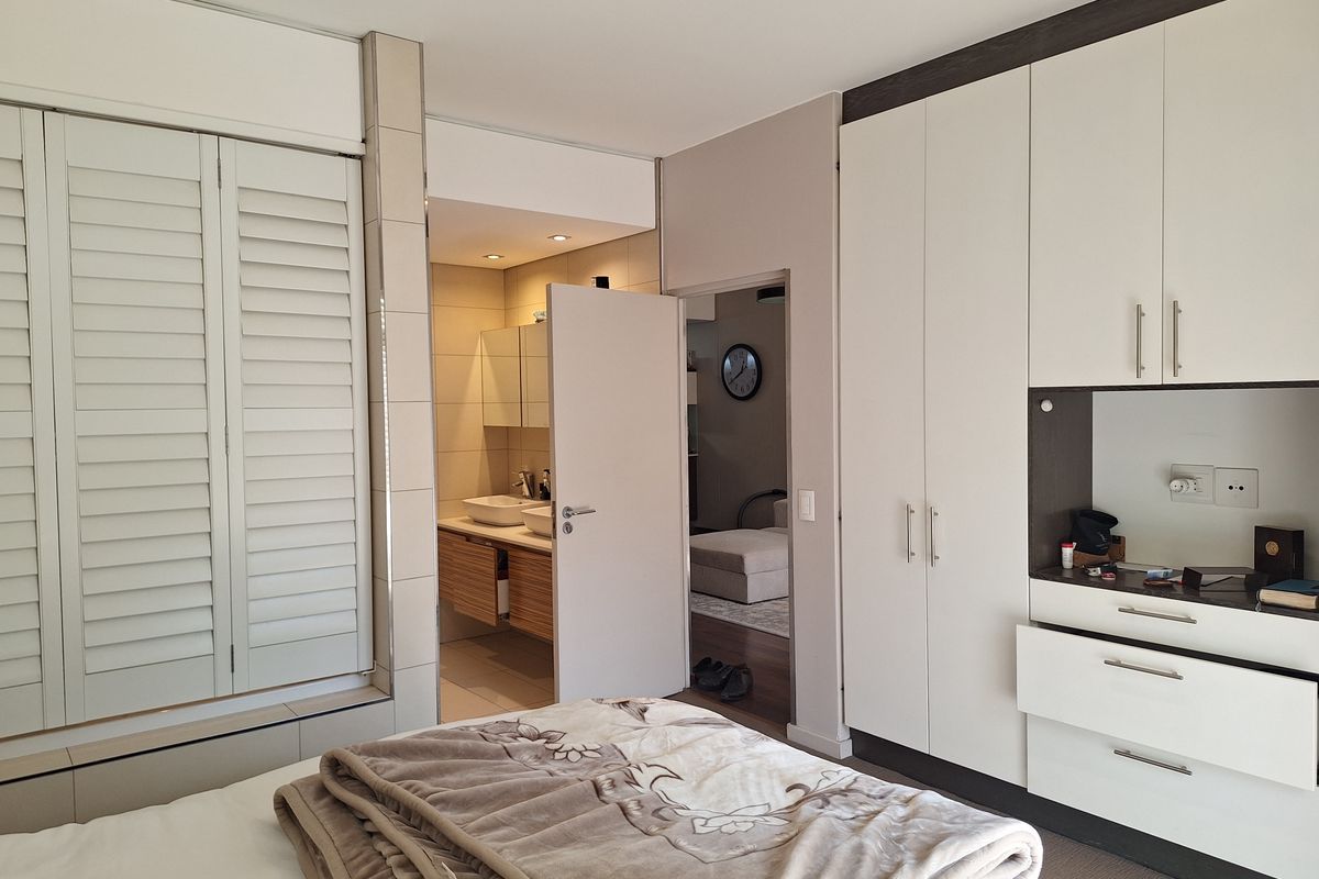 Spacious bedroom featuring extensive built-in cabinetry, shutter blinds, and direct access to a modern en-suite bathroom with dual vanity.