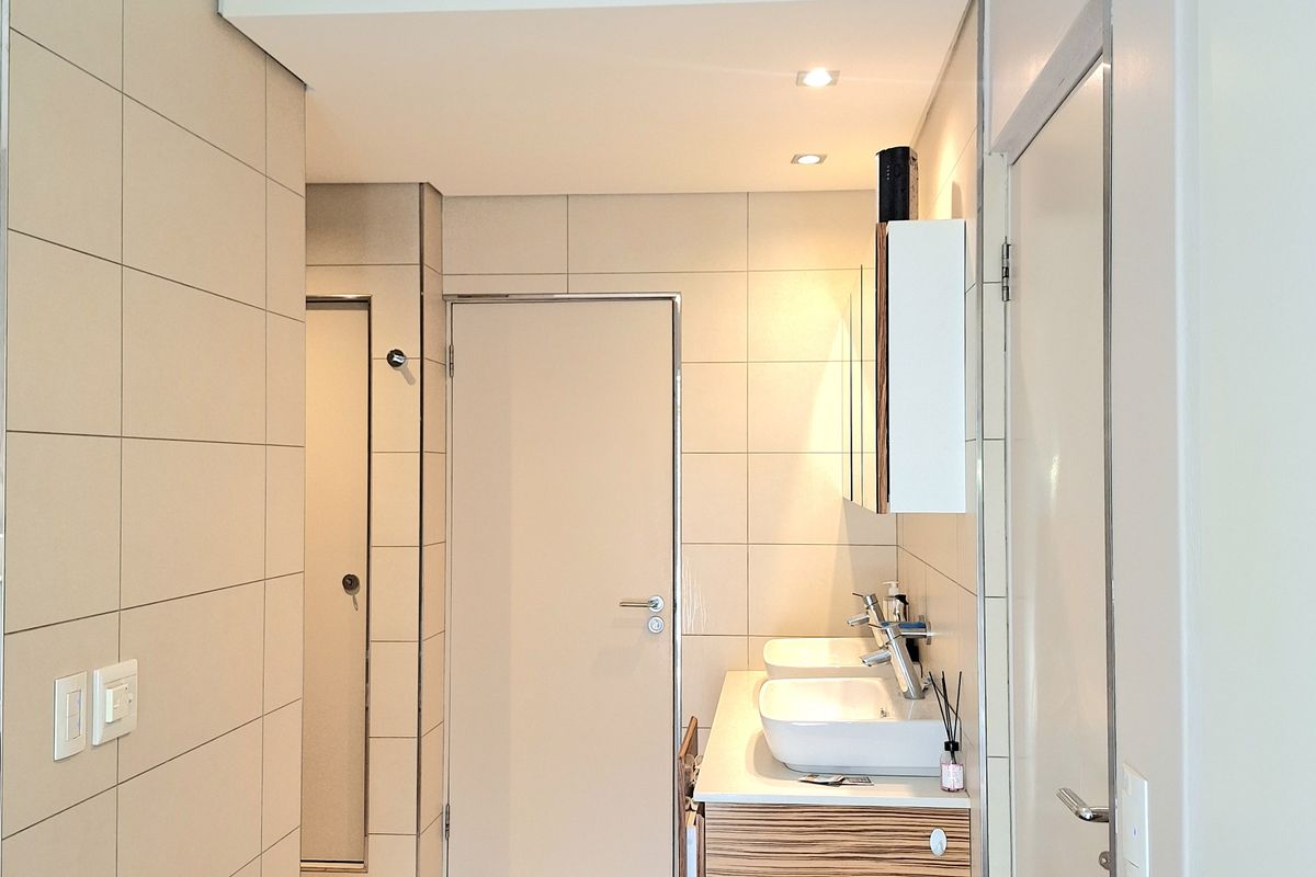 A modern bathroom featuring a double vanity with wall-mounted cabinetry, neutral tiled walls and flooring, and recessed lighting.
