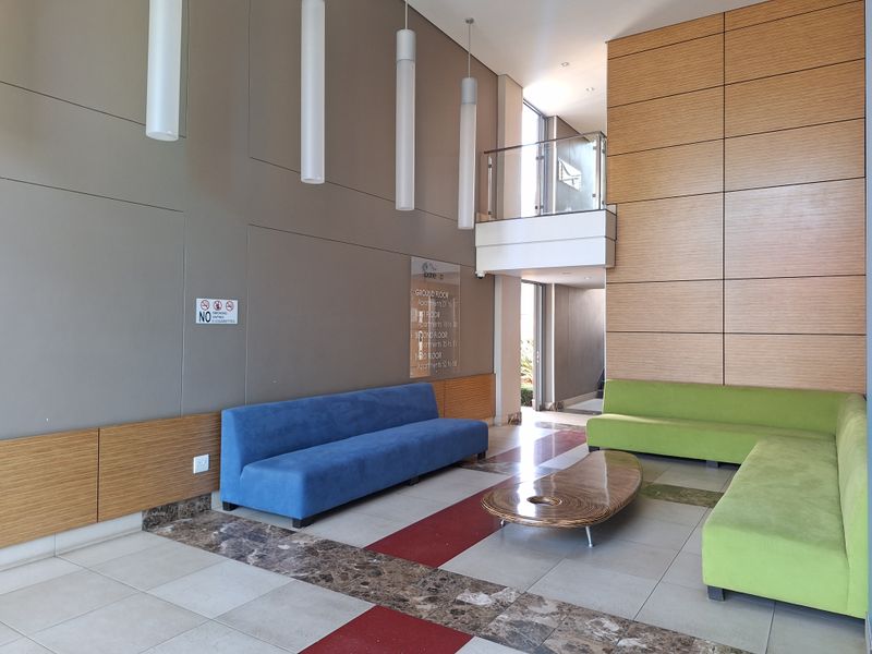 A modern, double-volume apartment building entrance lobby featuring wood-paneled walls, tiled flooring, and contemporary pendant lighting.