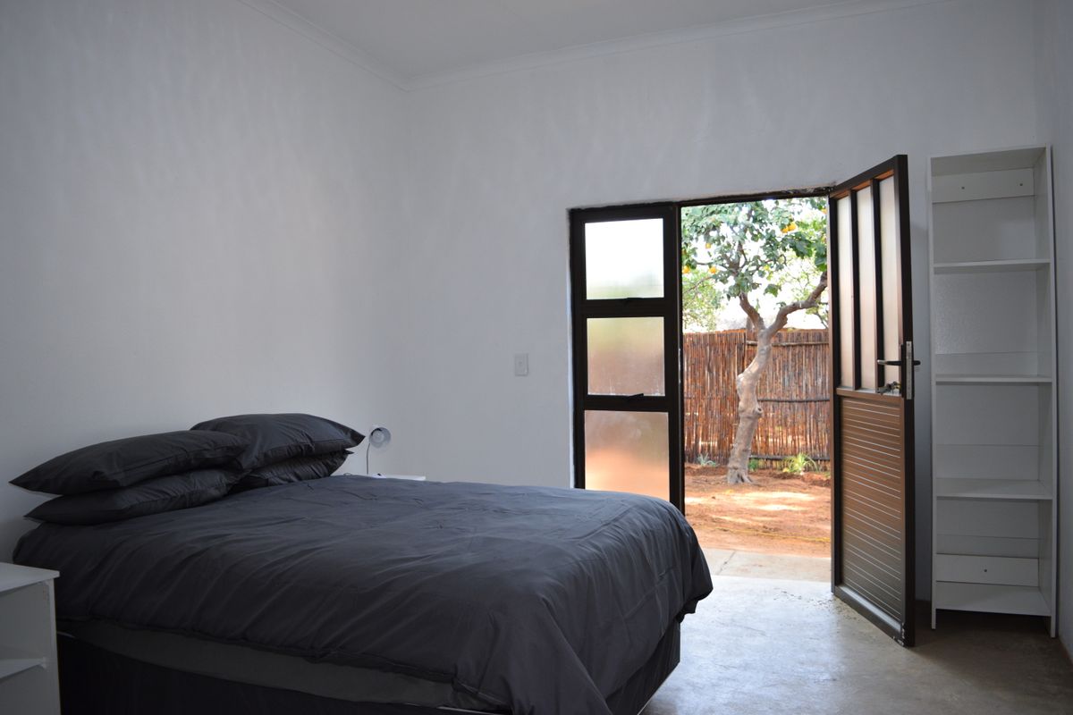 A bedroom featuring concrete flooring and a glass panel door providing direct access to an outdoor garden area.