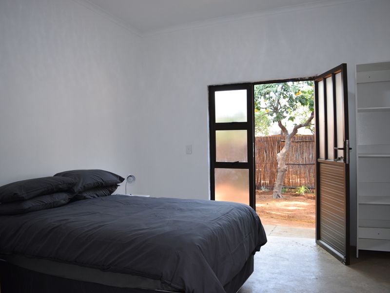 A bedroom featuring concrete flooring and a glass panel door providing direct access to an outdoor garden area.