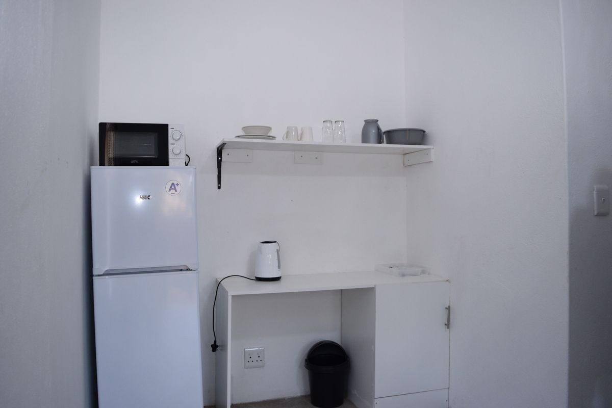 A compact kitchen area featuring basic white cabinetry, wall-mounted shelving, and dedicated space for a refrigerator.