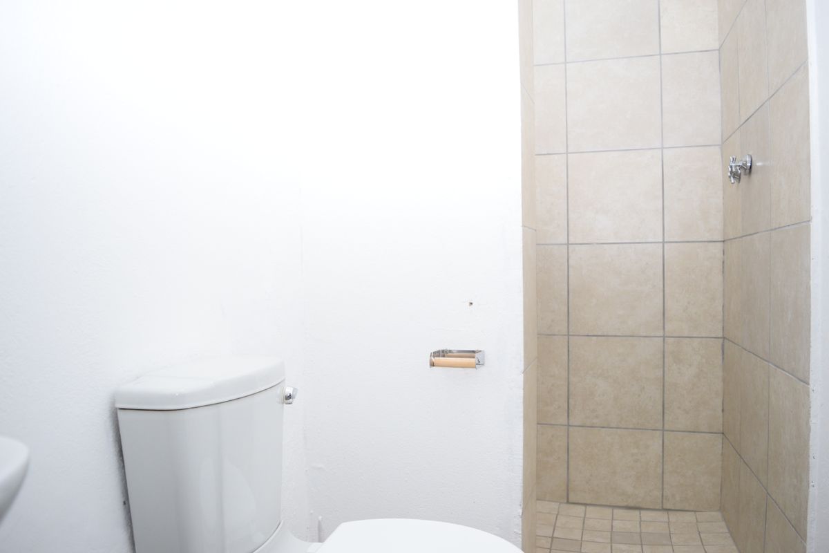 A functional bathroom featuring a standard toilet and a tiled shower enclosure with neutral wall and floor tiles.