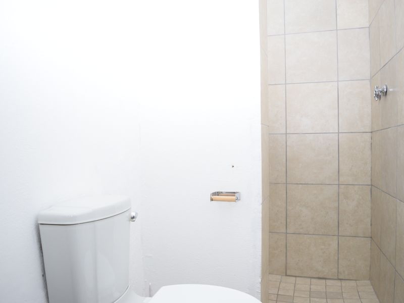 A functional bathroom featuring a standard toilet and a tiled shower enclosure with neutral wall and floor tiles.