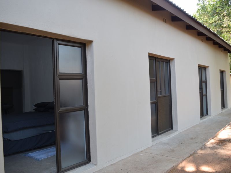 Rear exterior view of the apartment featuring a concrete walkway and multiple aluminium sliding doors providing access to the interior rooms.