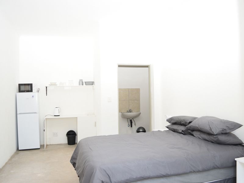 A compact bedroom featuring a built-in desk area, shelving, and an en-suite bathroom with a wall-mounted basin.