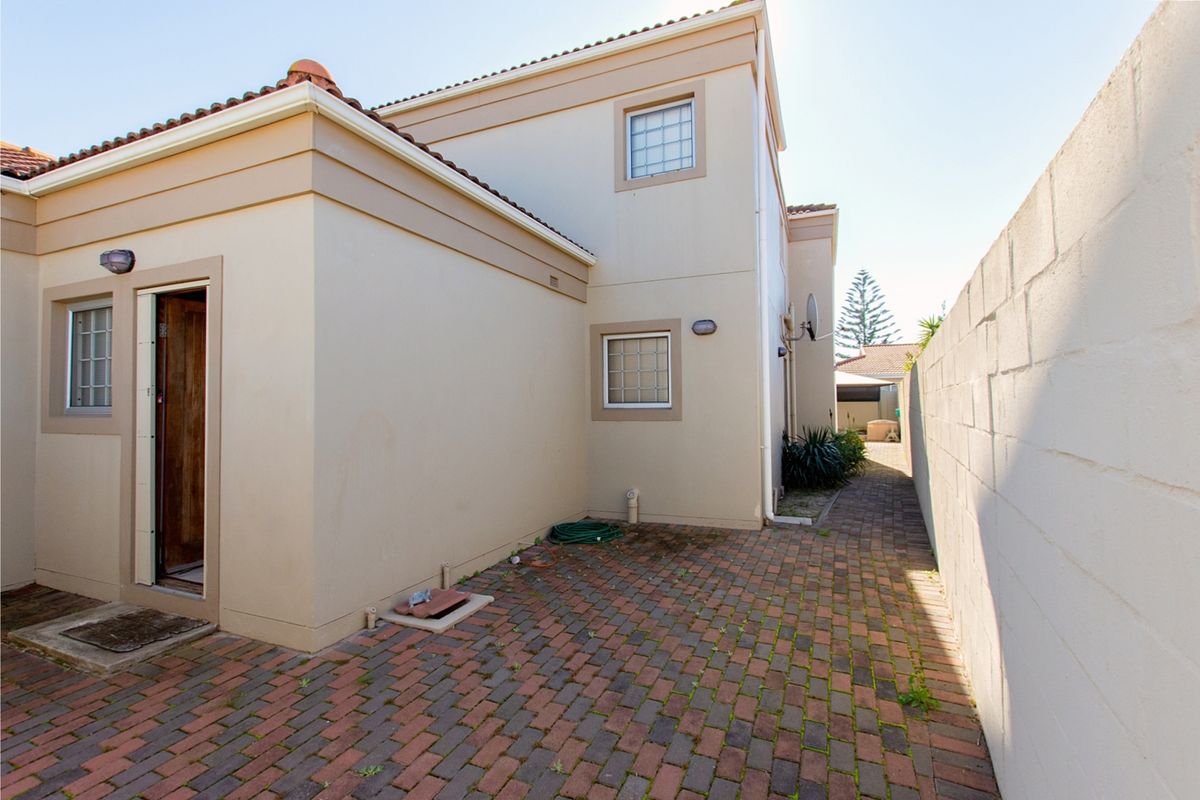 A side courtyard area featuring brick paving, a high boundary wall, and exterior access to the property.