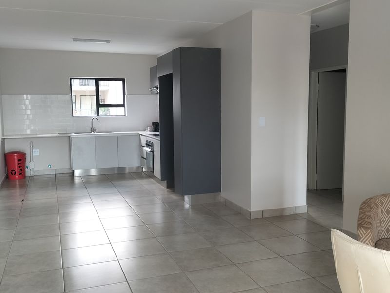 An open-plan living and kitchen area featuring neutral tiled flooring, modern grey and white cabinetry, and a built-in oven with a tiled backsplash.