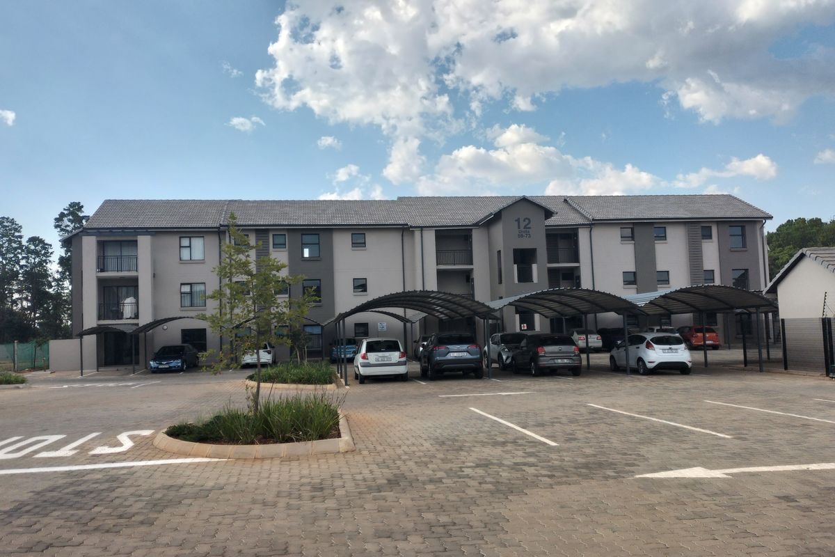 Front elevation of a multi-story apartment complex featuring paved parking areas, covered carports, and well-maintained building facades.