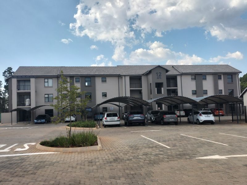Front elevation of a multi-story apartment complex featuring paved parking areas, covered carports, and well-maintained building facades.