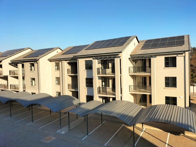 Exterior view of a modern apartment complex featuring multiple balconies, tiled roofing with integrated solar panels, and covered parking bays.