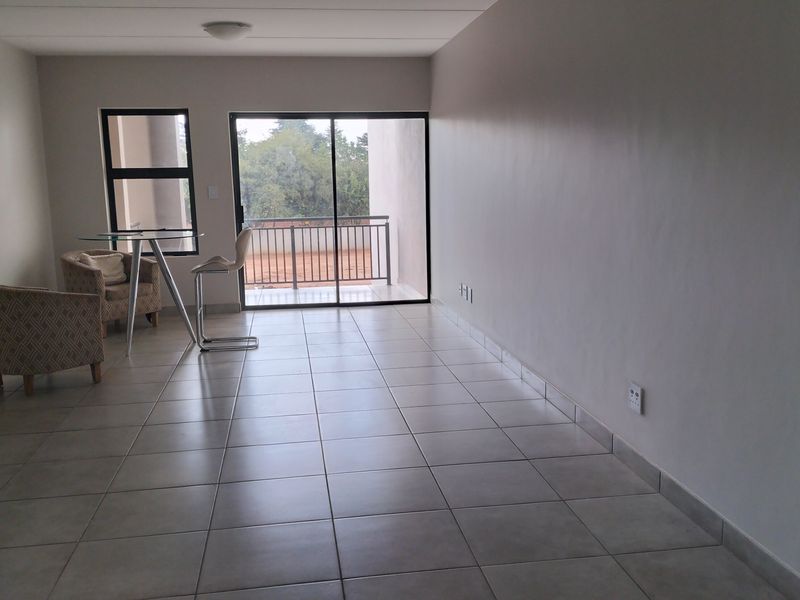 A spacious, light-filled living area featuring neutral tiled flooring and large sliding glass doors that provide direct access to an outdoor balcony.