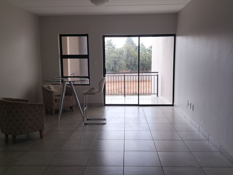 A spacious, neutrally finished living area featuring tiled flooring and a large sliding glass door that opens onto a private balcony.