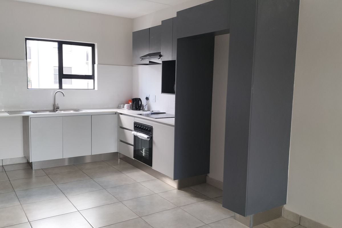 Modern kitchen featuring sleek white and grey cabinetry, built-in oven with hob, extractor fan, and tiled flooring in a clean, contemporary layout.