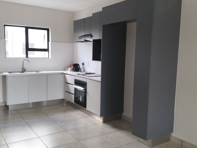 Modern kitchen featuring sleek white and grey cabinetry, built-in oven with hob, extractor fan, and tiled flooring in a clean, contemporary layout.