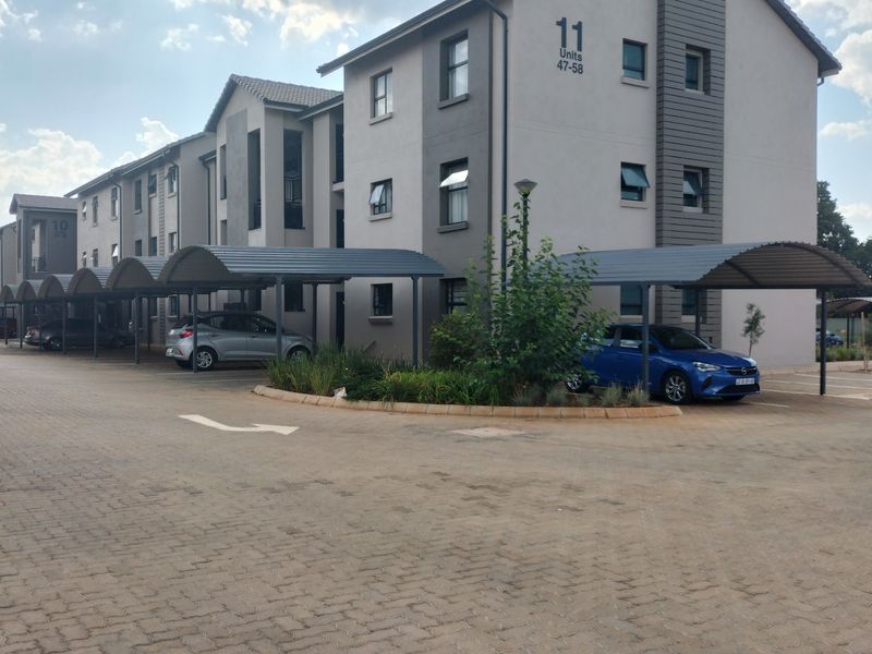 Exterior view of a modern apartment complex featuring paved parking areas, covered carports, and well-maintained building facades.