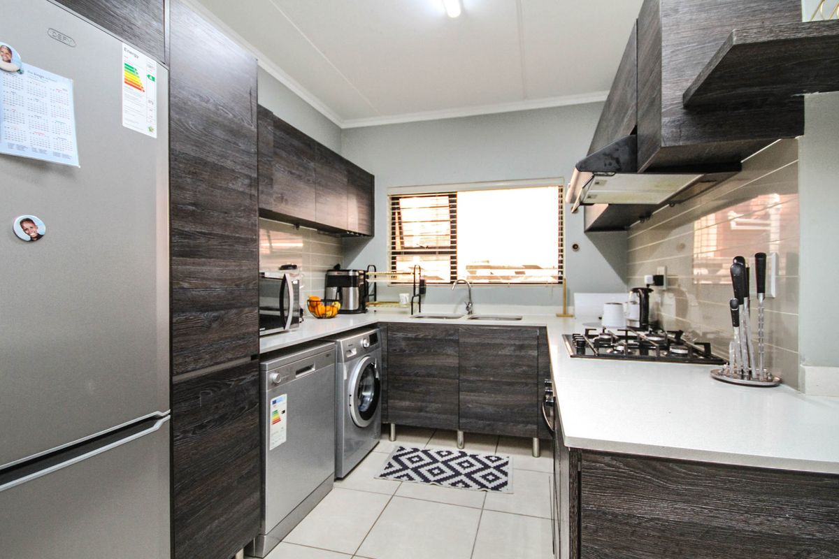 Modern kitchen featuring dark wood-grain cabinetry, stone-look countertops, gas hob, extractor fan, and integrated space for laundry appliances.
