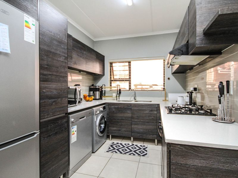 Modern kitchen featuring dark wood-grain cabinetry, stone-look countertops, gas hob, extractor fan, and integrated space for laundry appliances.