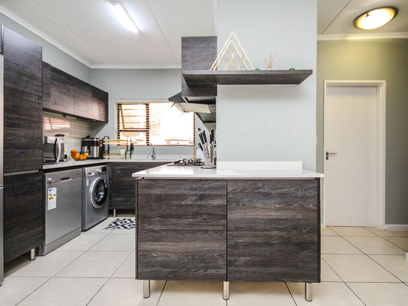 Modern kitchen featuring dark wood-grain cabinetry, a central island, tiled flooring, and integrated appliances including a gas hob and extractor fan.