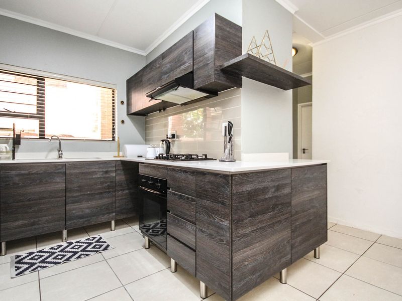 Modern kitchen featuring dark wood-grain cabinetry, built-in oven, gas hob, extractor fan, and light-toned tiled flooring with ample counter space.
