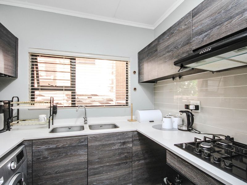 Modern kitchen featuring dark wood-grain cabinetry, stone countertops, a double sink, gas hob, and integrated extractor fan with a tiled backsplash.