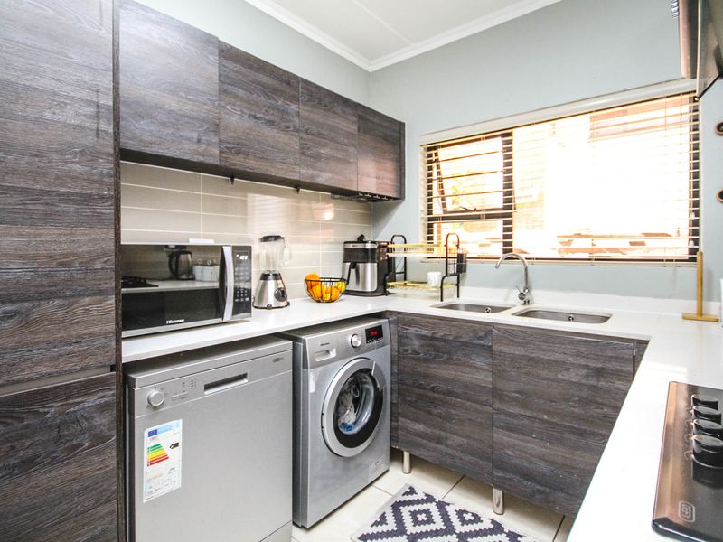 Modern kitchen featuring dark wood-grain cabinetry, stone countertops, a double basin sink, and integrated hob with extractor fan.