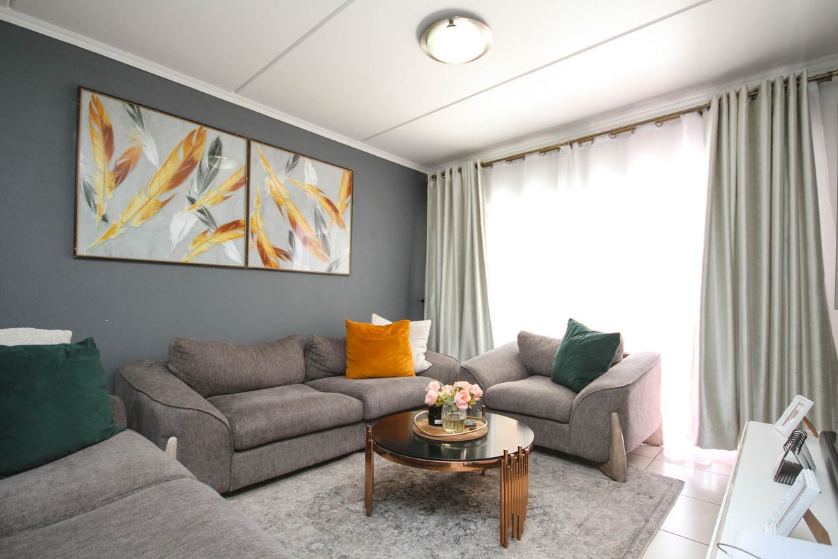 A well-maintained living room featuring tiled flooring, neutral wall tones, and large windows with curtain tracks, providing a comfortable and bright living space.