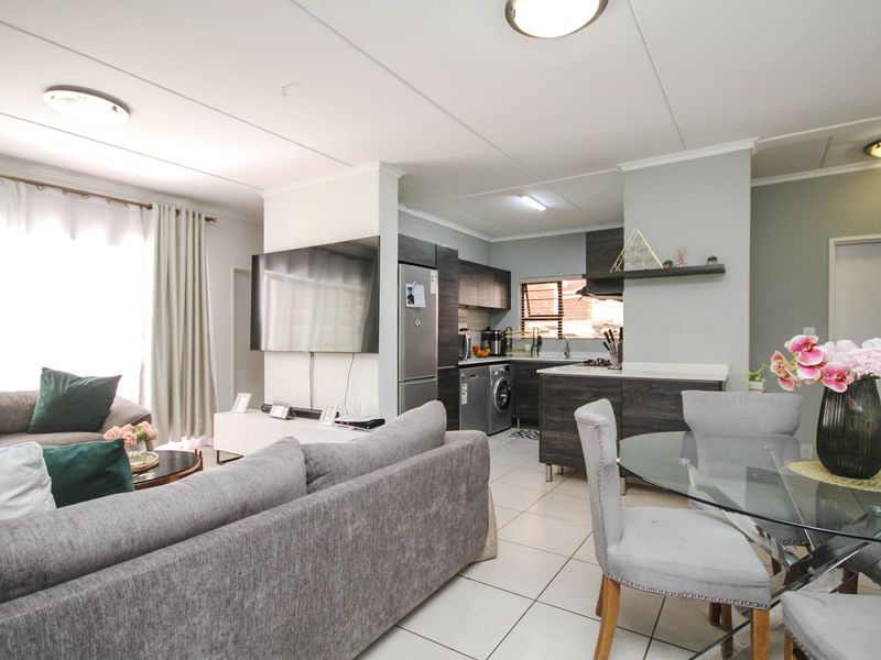 An open-plan living and kitchen area featuring tiled flooring, modern dark-toned cabinetry, and integrated kitchen appliances, creating a functional and cohesive living space.
