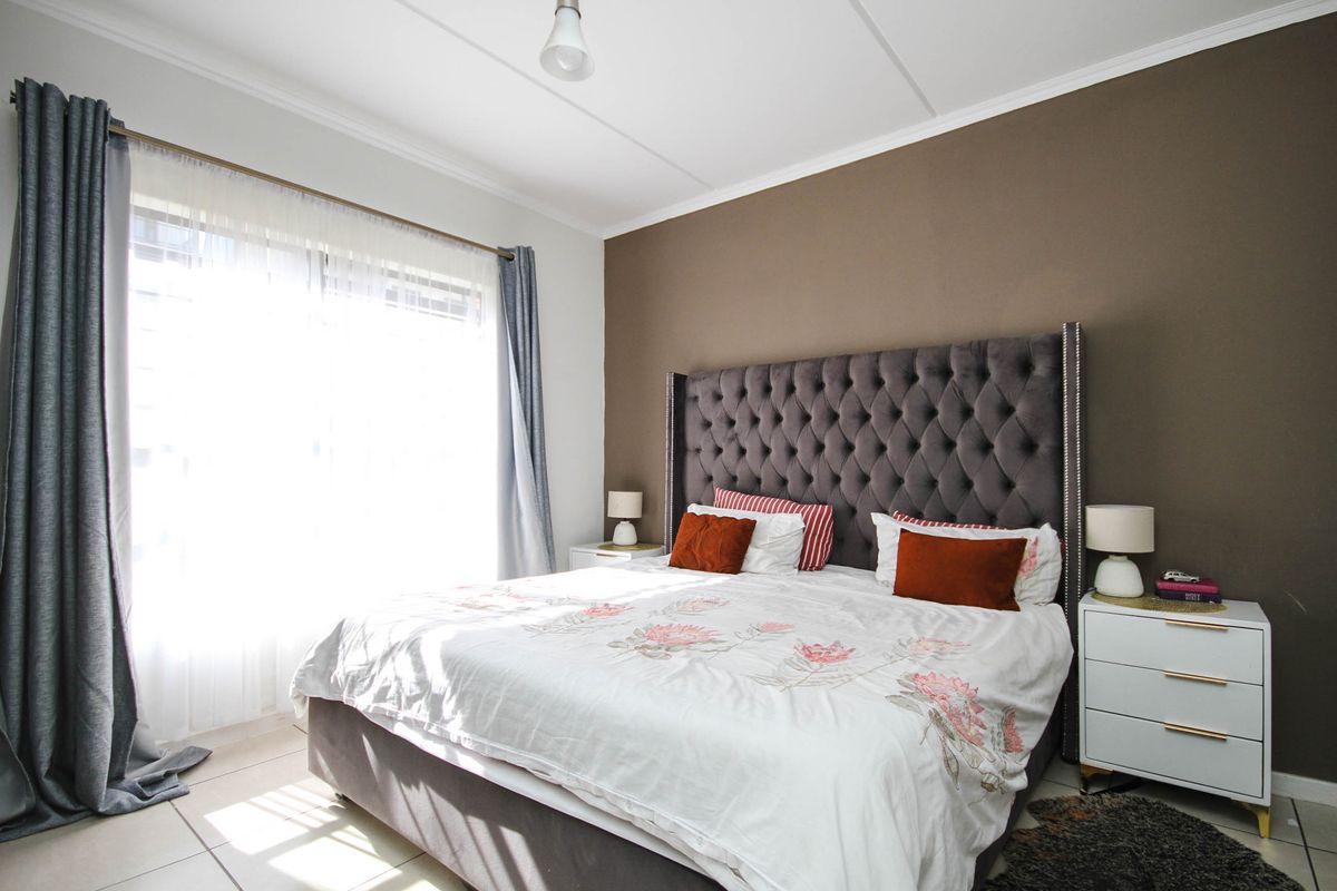 A well-lit bedroom featuring neutral tiled flooring, a large window with natural light, and a feature wall.