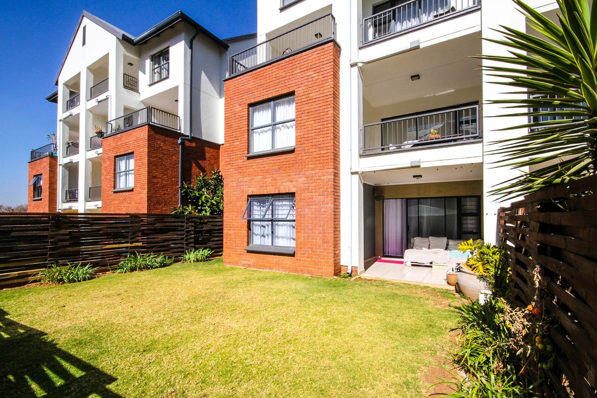 Rear view of the apartment building featuring a private garden, tiled patio area, and multi-level balconies with brick and white render finishes.