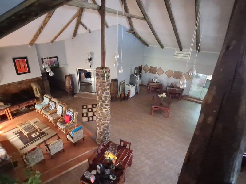 Spacious open-plan living and dining area featuring high vaulted ceilings with exposed timber trusses, a stone-clad central column, and tiled flooring.