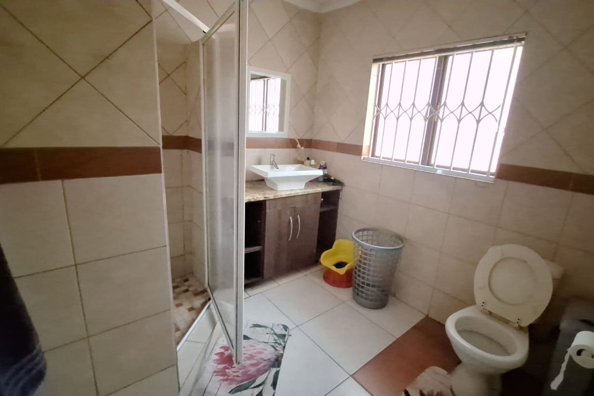 A functional bathroom featuring a shower enclosure, vanity with vessel sink, toilet, and tiled finishes throughout.