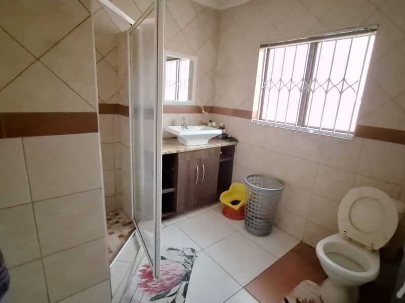 A functional bathroom featuring a shower enclosure, vanity with vessel sink, toilet, and tiled finishes throughout.