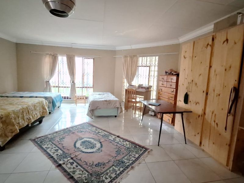 Spacious bedroom featuring tiled flooring, built-in wooden wardrobes, and security bars on the windows, offering a functional and well-lit living space.